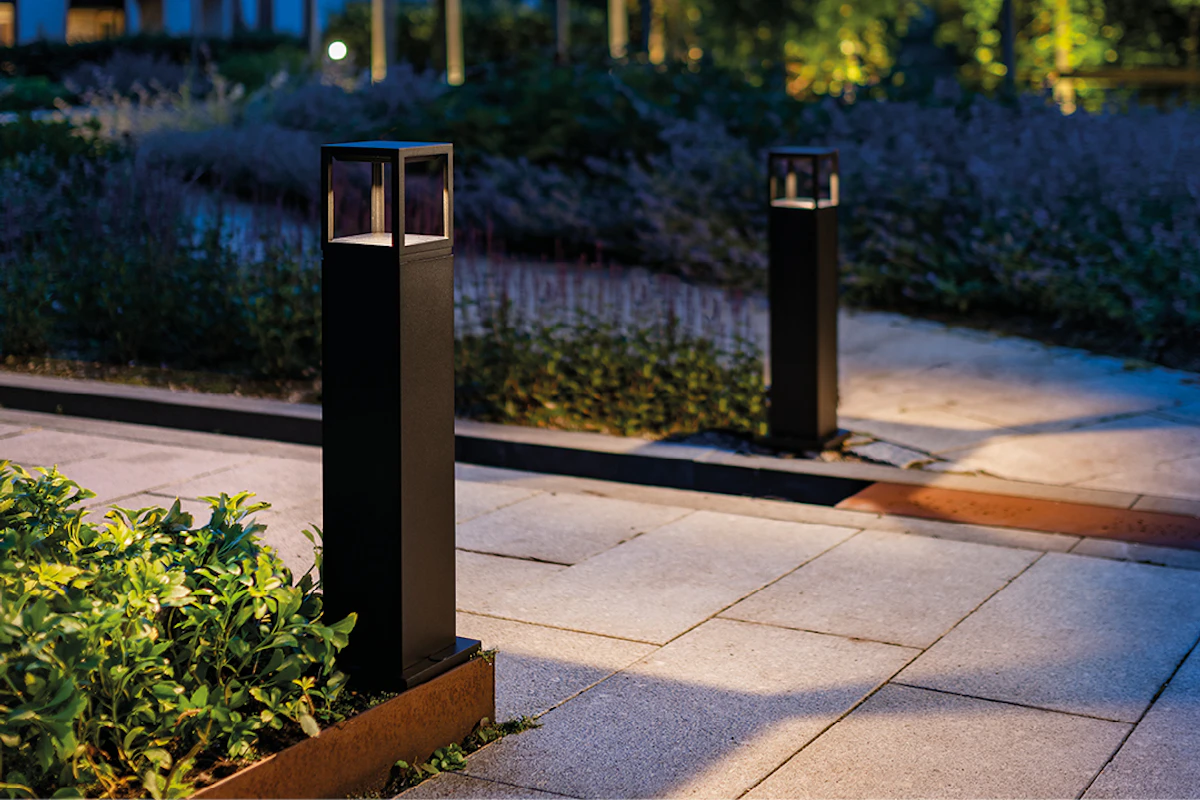 Bildet viser 2 stykk av pullerten Fagernes Bollard, som lyser opp på hver sin side av en steinbelagt gangvei. Foto.