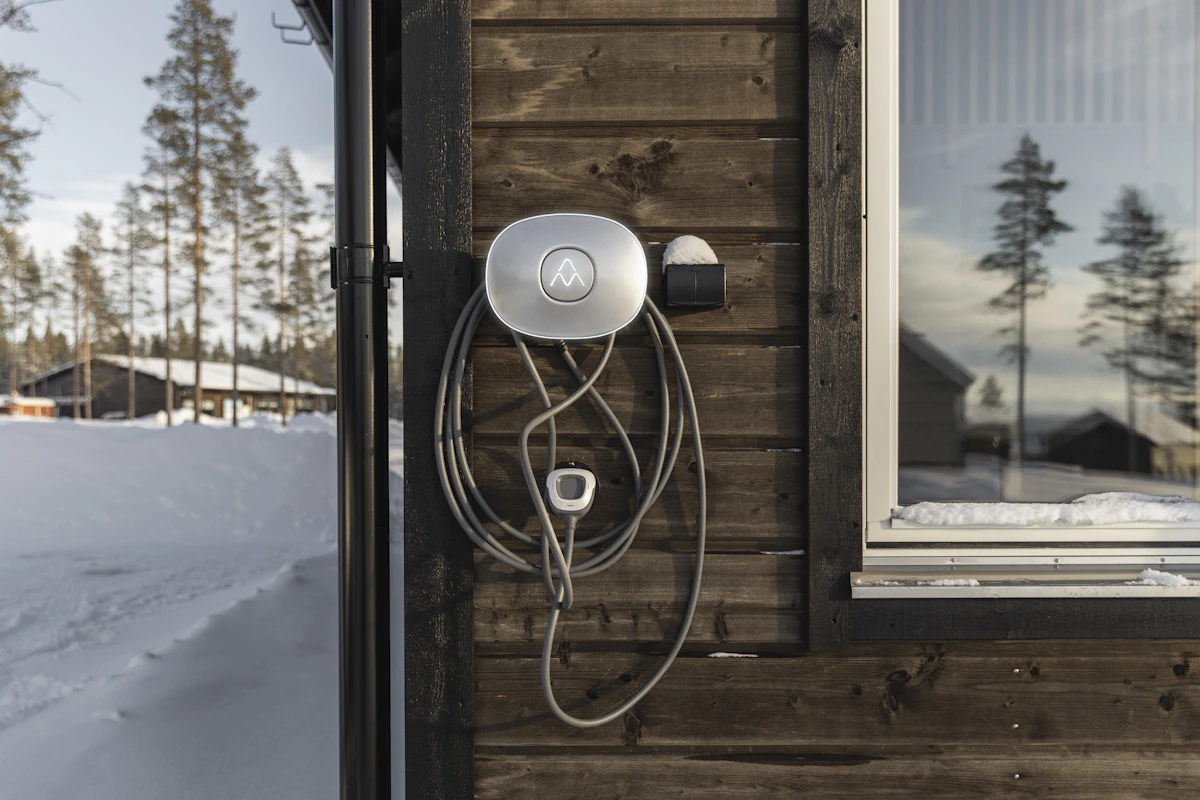 Charge Amps elbillader montert på hyttevegg med snø i omgivelsene. Foto.