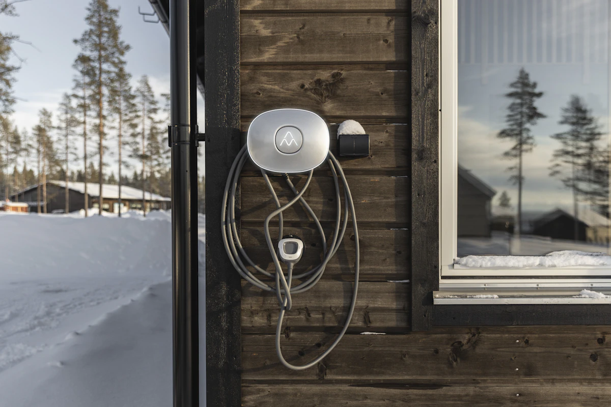 Charge Amps elbillader montert på hyttevegg med snø i omgivelsene. Foto.