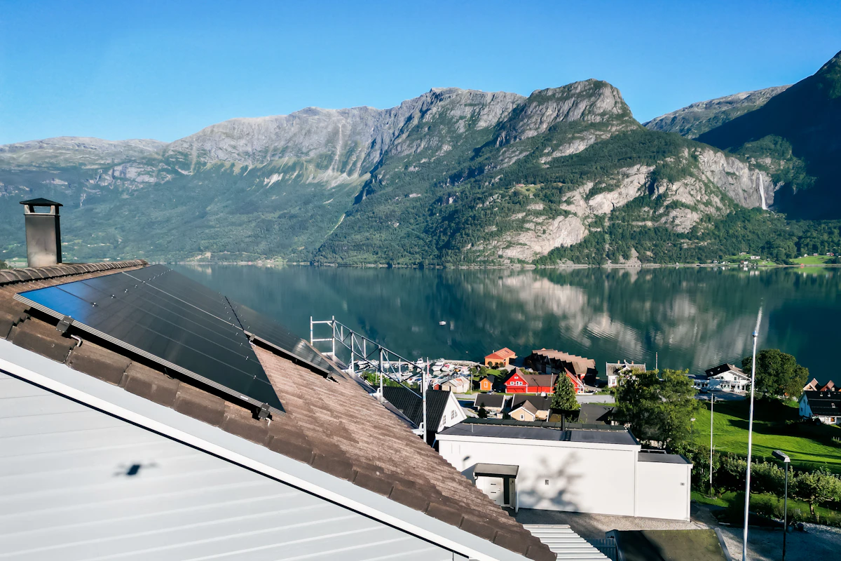 Solcelleanlegg, tatt fra siden på et bolighus, med utsikt over fjord og fjell. Dronefoto