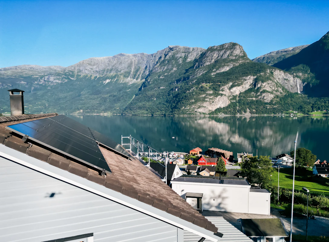 Solcelleanlegg, tatt fra siden på et bolighus, med utsikt over fjord og fjell. Dronefoto