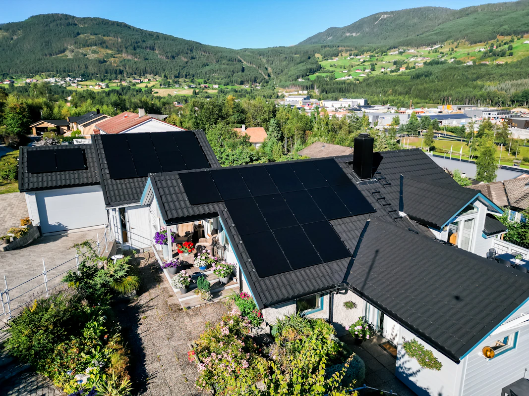 Sorte solceller på taket på en bolig og på to av påbyggene. Dronefoto