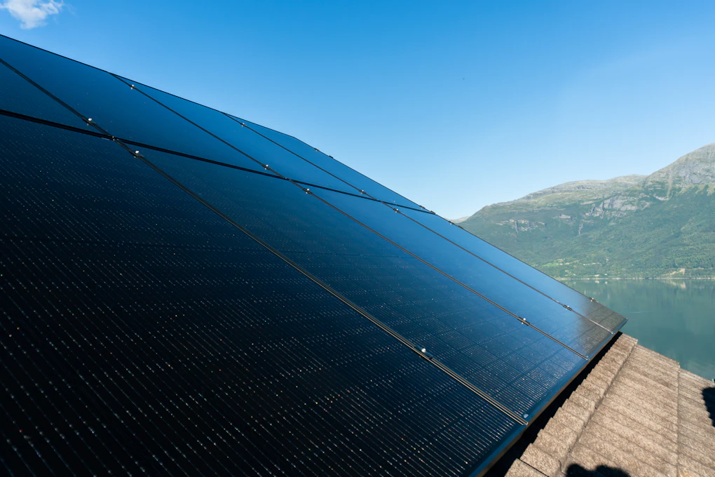 Åtte store solcellepanel på taket sett fra siden, fjord i bakgrunnen. Foto