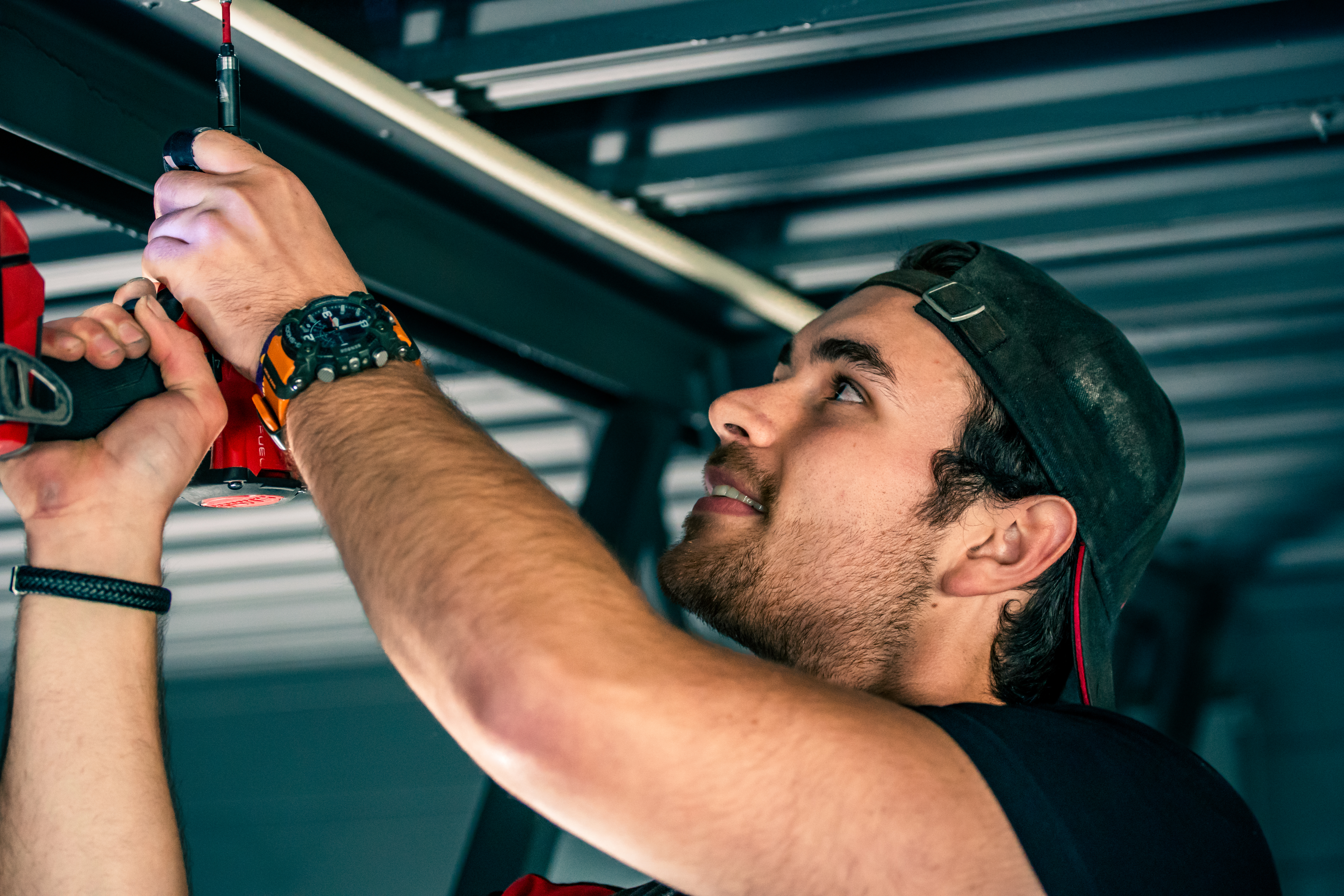 Elekstirker skrur fast rør til ledningene i taket på et industribygg. Foto.