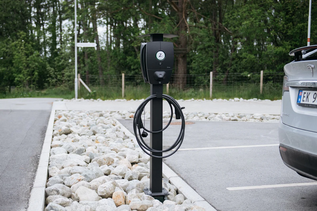 Bildet viser en Tesla som er parkert ved siden av en stolpe med Zaptec Pro elbillader. Foto.