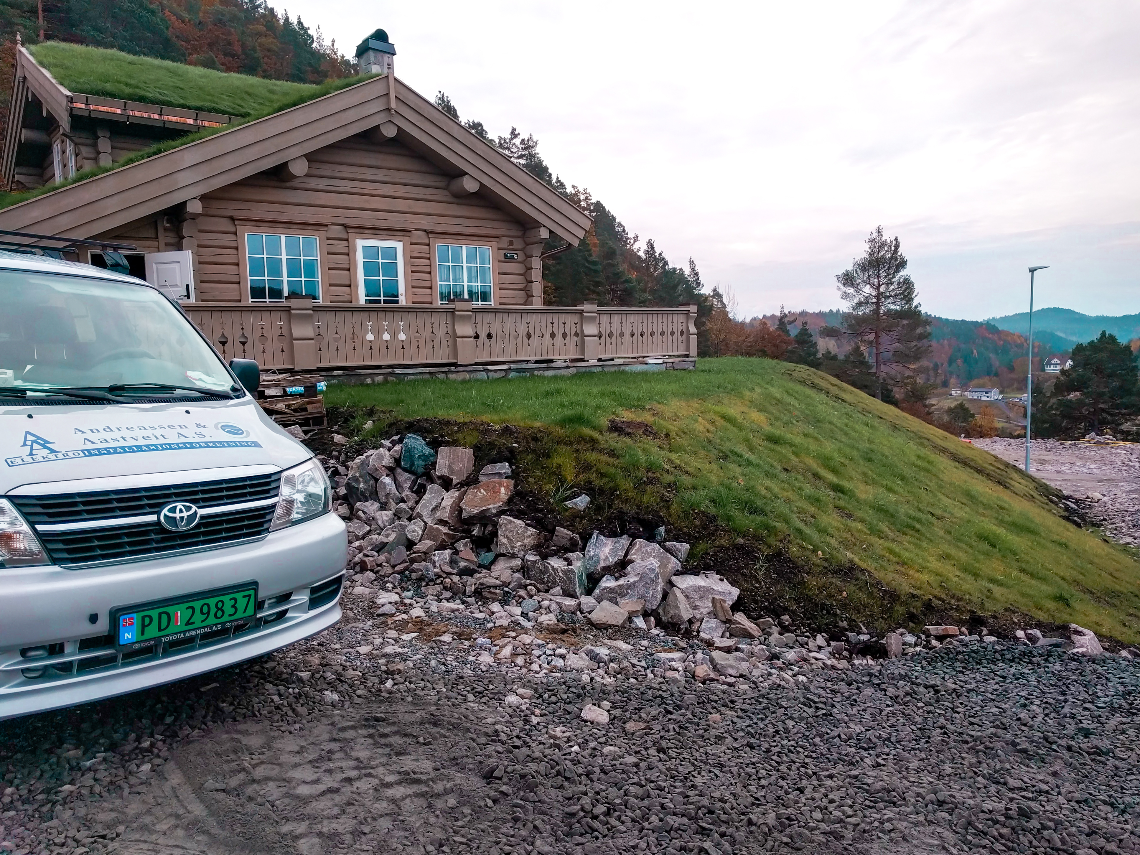 Andreassen & Aastveit AS bil står ved hytte. Foto.