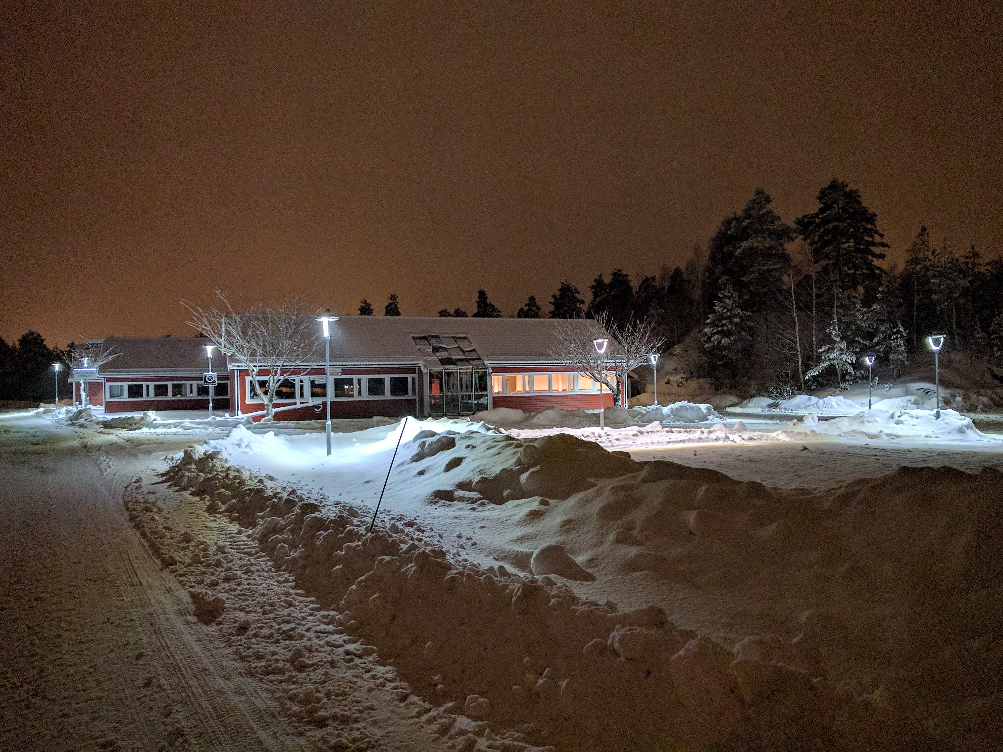 Gatelys som lyser opp område rundt en større bygning. Her i mørket og snøværet. Foto.