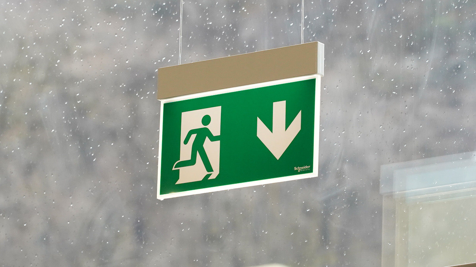 Nødlys i serien Exiway fra Schneider Electric, som henger i et vindu. Foto.