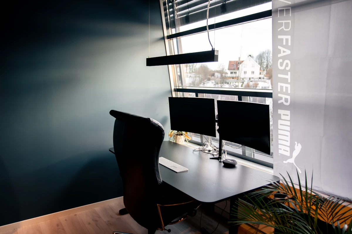 Lysarmatur over en kontorpult med to skjermer. Foto.