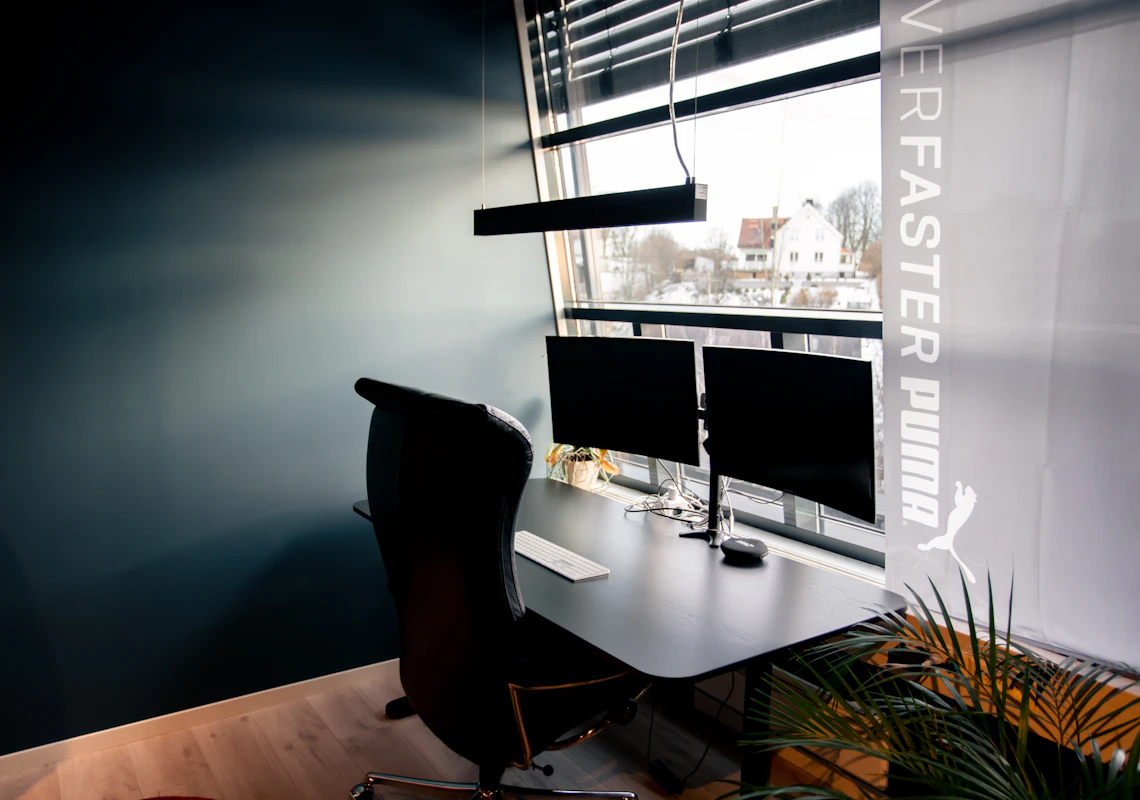 Lysarmatur over en kontorpult med to skjermer. Foto.