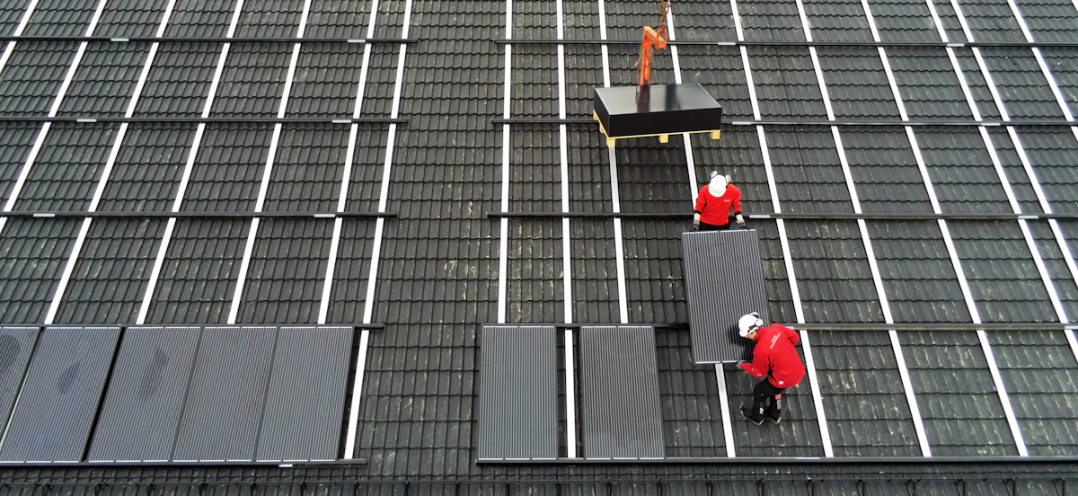 Bilde av tre ansatte i Folldal Elektro som bærer solcellepanel på tak