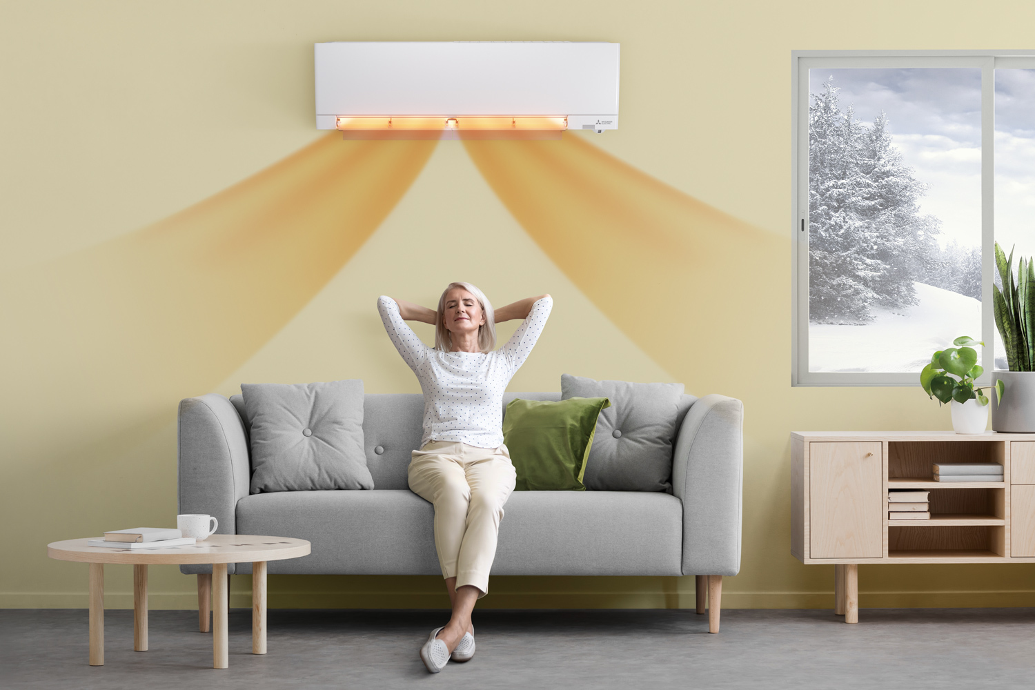 Mitsubishi Electric varmepumpe med toppmodellen UWANO i fargen hvit plassert over sofaen med en dame sittende komfortabelt og uforstyrret av pumpen. Bilde